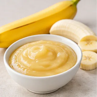 Smooth banana purée in a bowl beside bananas