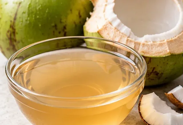 Coconut water in a clear glass beside fresh coconuts